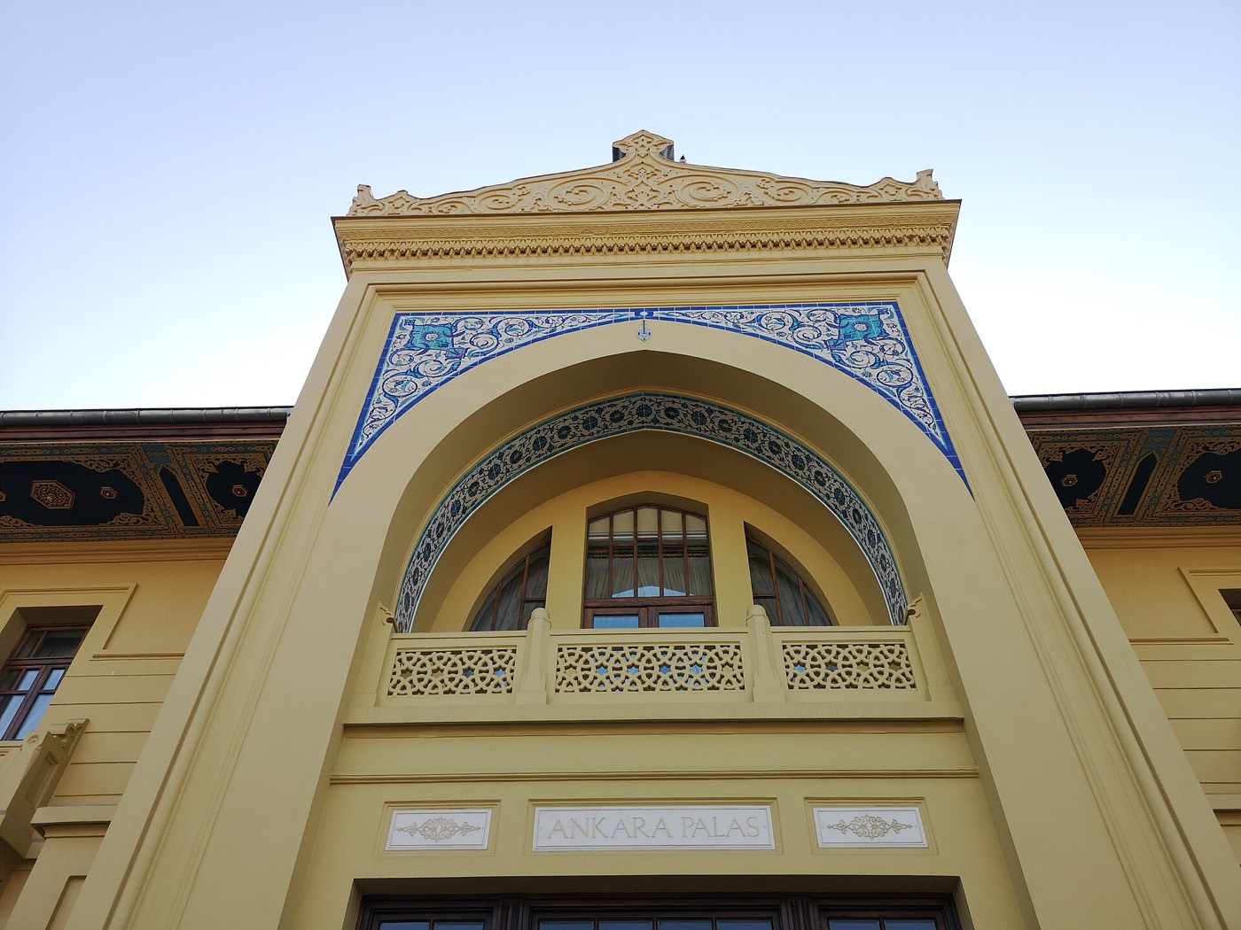 The pointed arch over the main entrance of Ankara Palas, framed with blue and white tiles above a carved stone balcony and the building's name