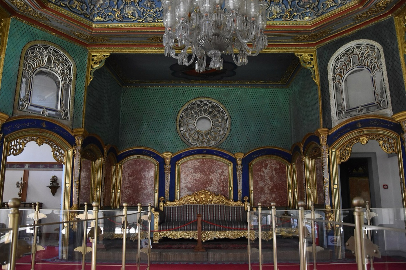 A room in Aynalıkavak Pavilion with green walls, a gilded sofa set in an alcove behind a rope barrier, openwork window grilles and a crystal chandelier