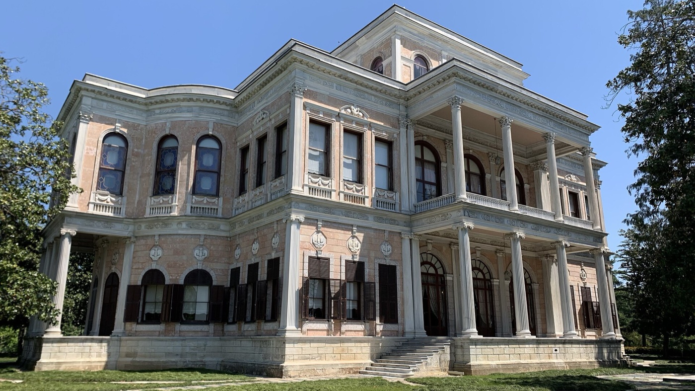 Beykoz Mecidiye Pavilion on a lawn: a two-storey building with a columned porch on both floors at one corner and a flight of steps to the ground floor