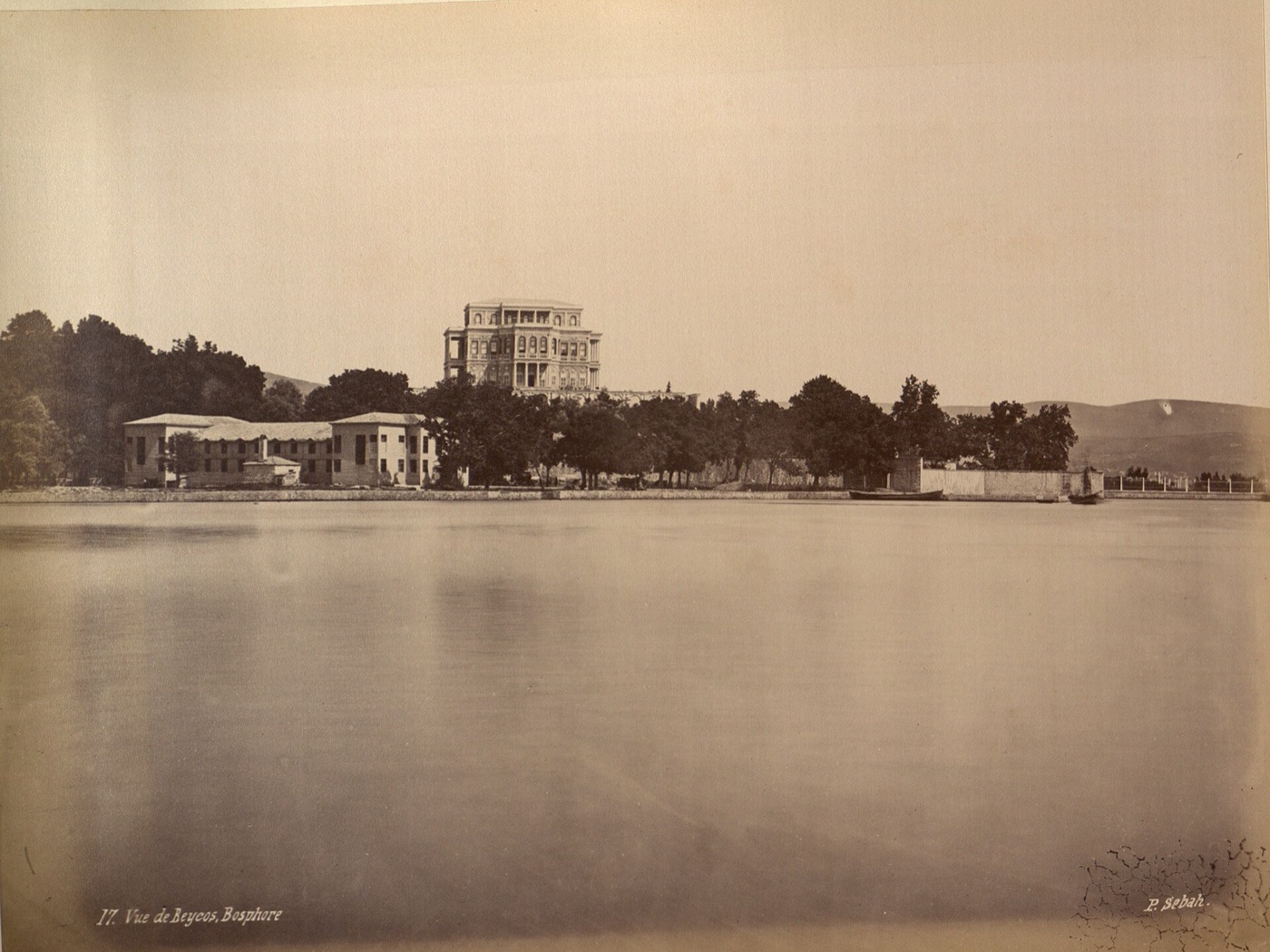 A nineteenth-century photograph titled Vue de Beycos, Bosphore: the pavilion stands on high ground above trees, with low buildings and a sea wall along the shore in front
