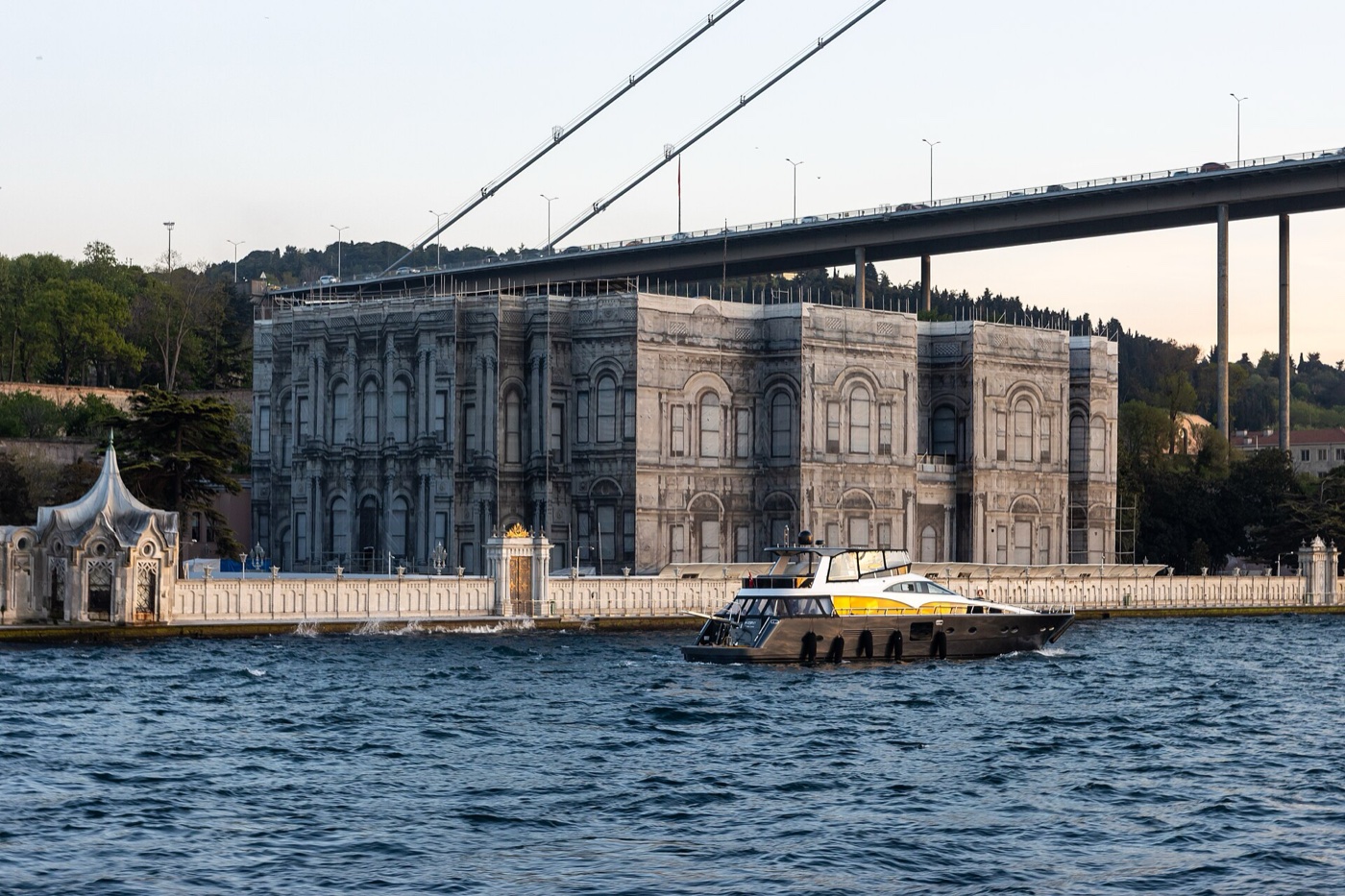 Beylerbeyi Palace seen from the Bosphorus, with a sea kiosk on the waterfront wall to the left and the deck of the Bosphorus bridge passing above