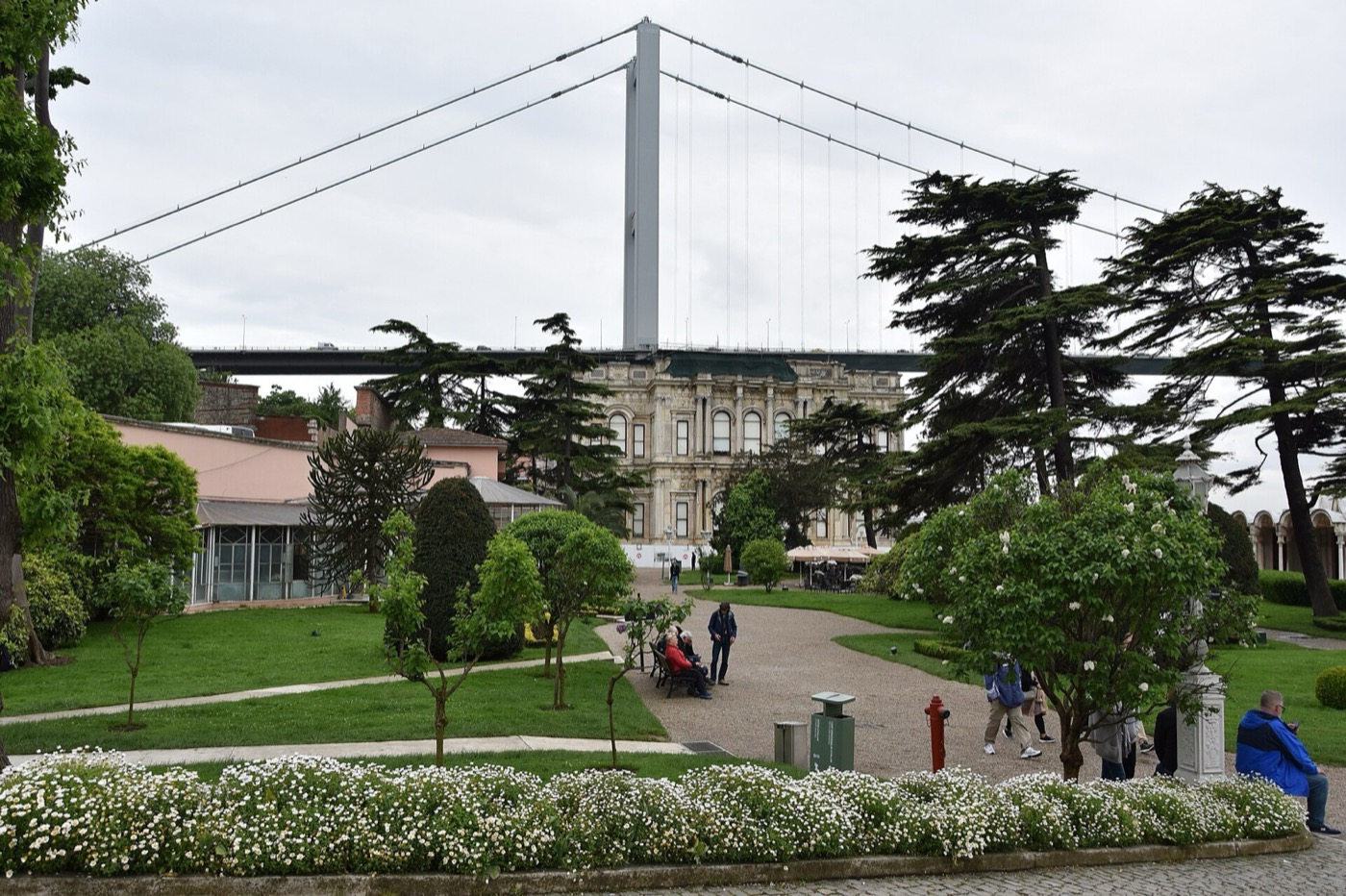 The garden of Beylerbeyi Palace with lawns, paths and tall cedars, the palace beyond and the Bosphorus Bridge passing overhead
