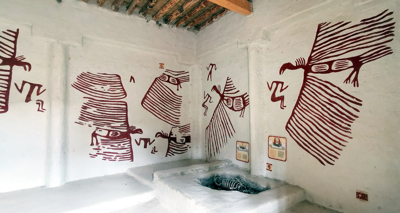 The reconstructed Neolithic house at Çatalhöyük: red wall paintings, a raised platform, and a burial cut into the floor beneath it
