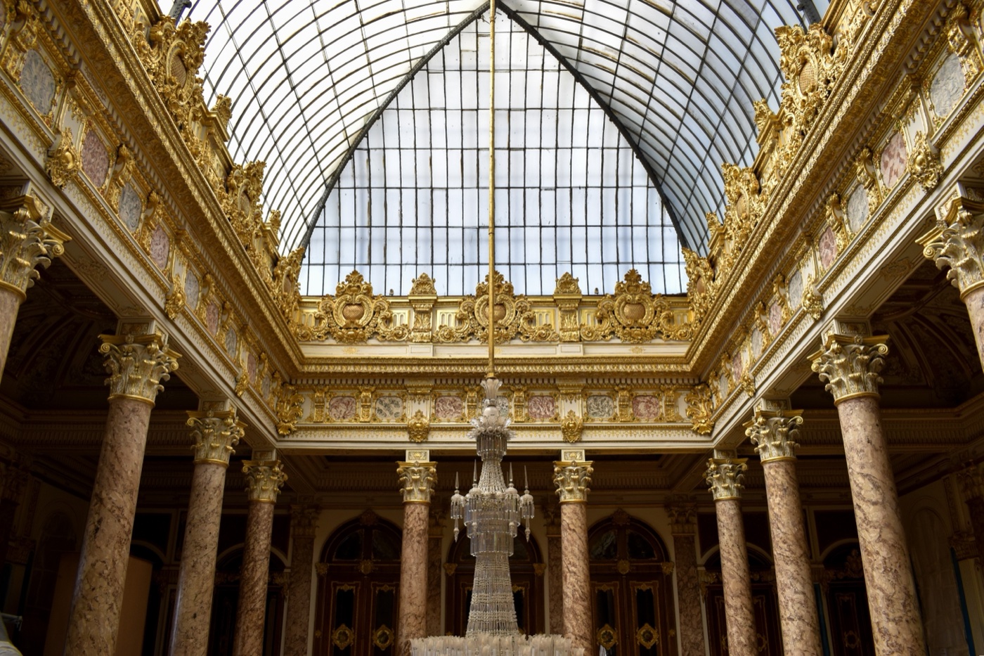 The glass-roofed hall of the Crystal Staircase in Dolmabahçe Palace, with gilded cornices, veined marble columns and a crystal chandelier hanging from the skylight