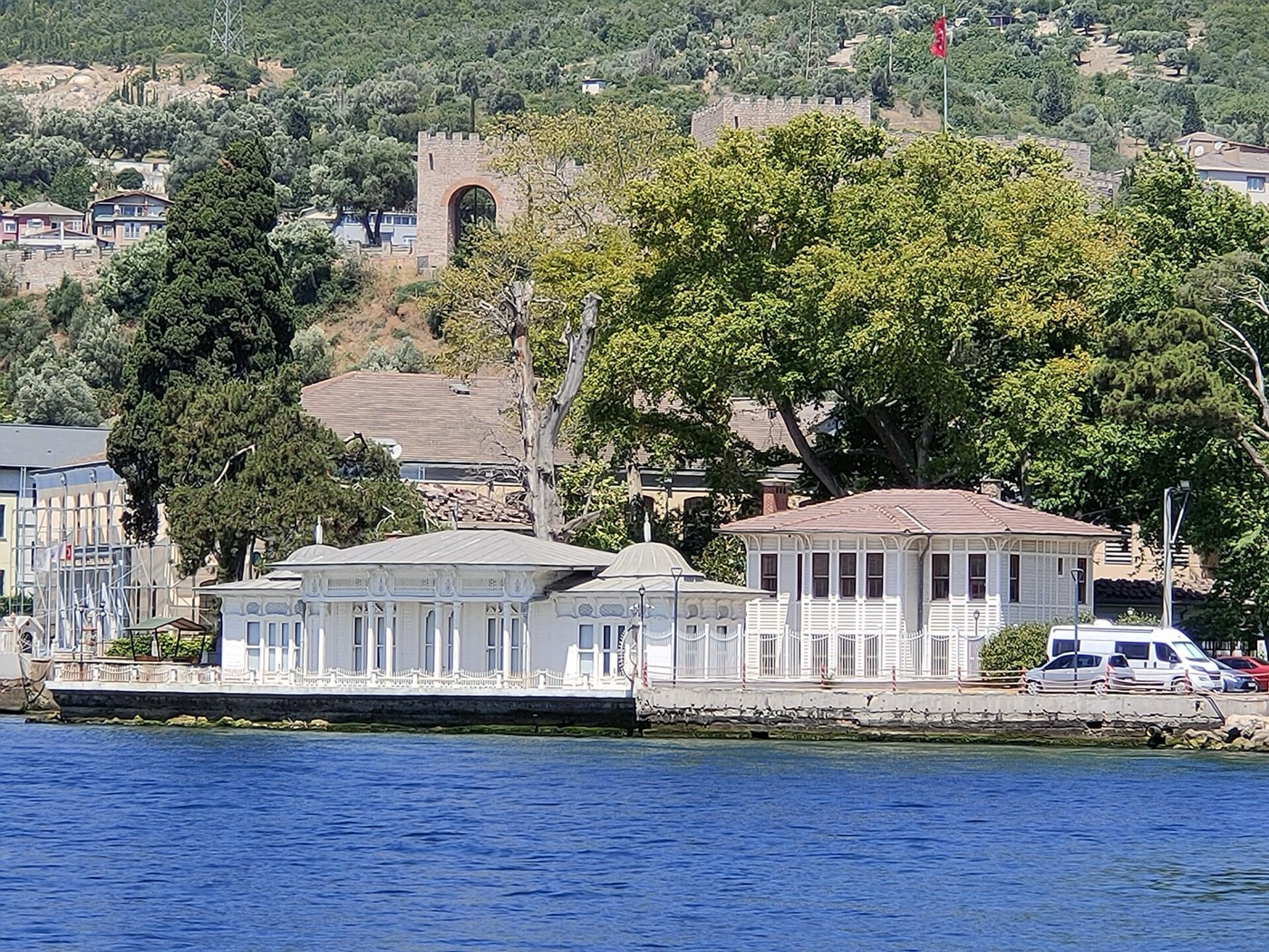 The Hereke waterfront seen from the sea, with the low white Kaiser Wilhelm Pavilion on the quay and the hillside town behind it