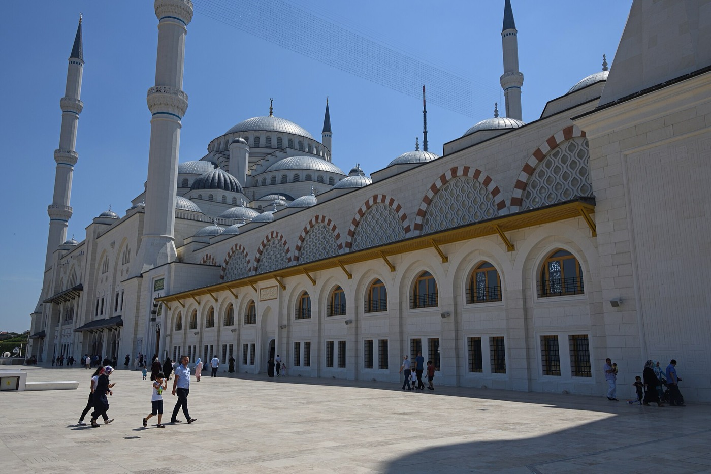 The Büyük Çamlıca Mosque seen from the northeast across its stone platform, with visitors walking past the arcaded side wall; the museum is part of this complex