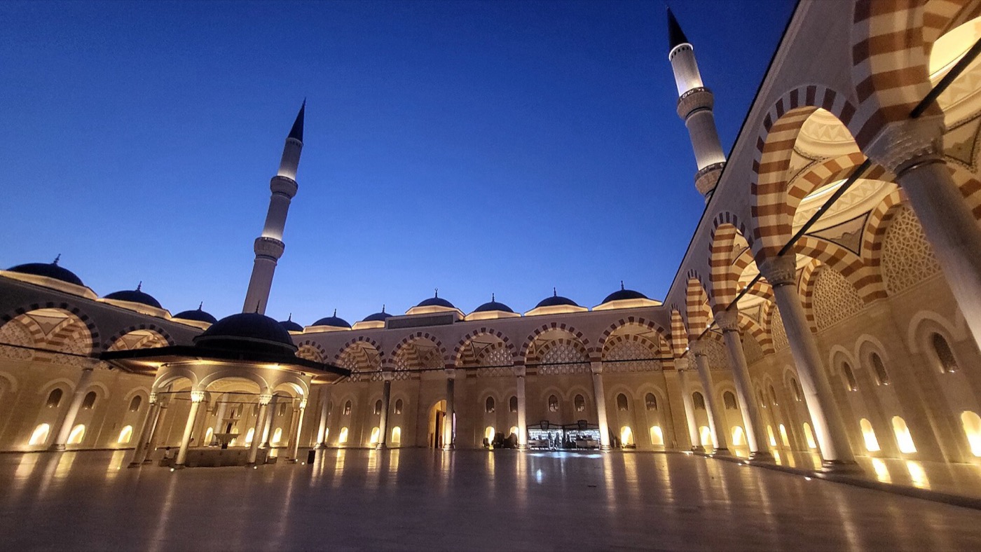 The courtyard of the Büyük Çamlıca complex at dusk, its striped arcades and fountain lit beneath two minarets
