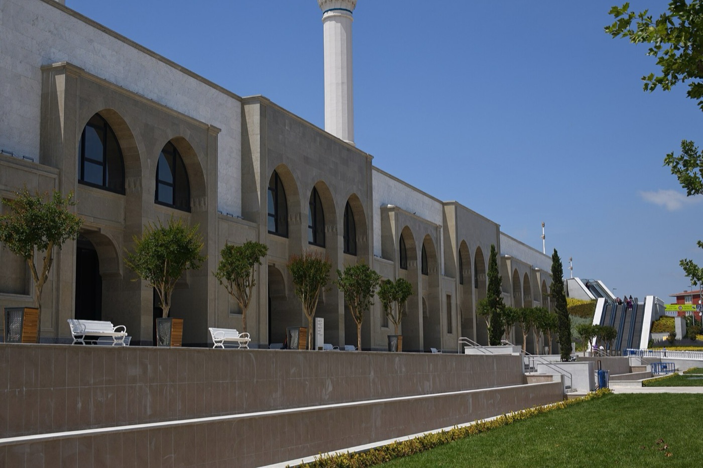 The arcaded lower storey of the Büyük Çamlıca complex below the raised platform, with a garden strip and a minaret above