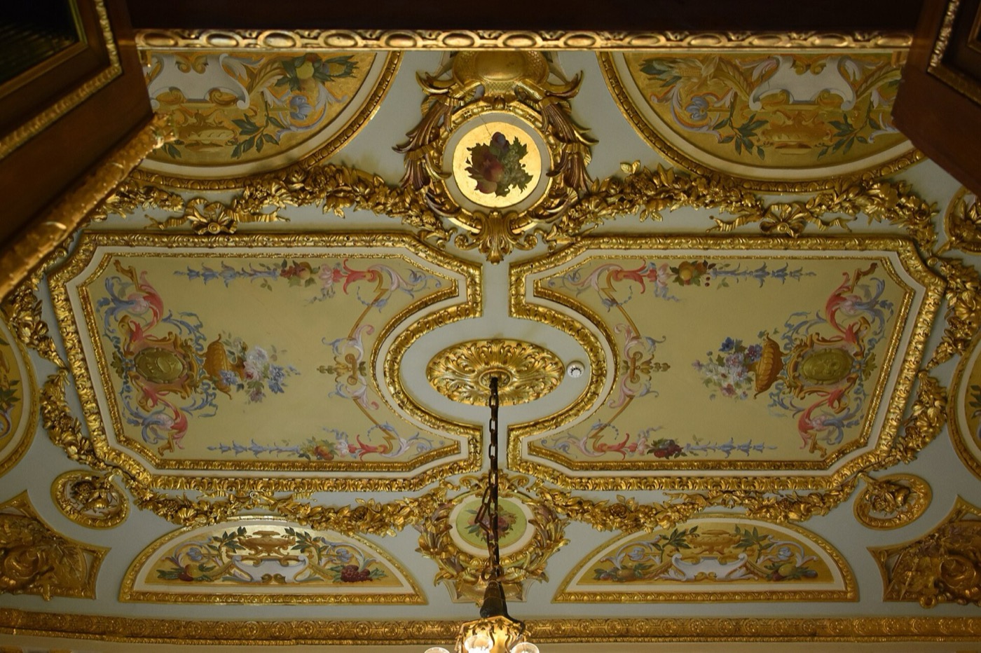 A ceiling in Küçüksu Pavilion: gilded mouldings framing painted floral panels around a central rosette from which a chandelier hangs