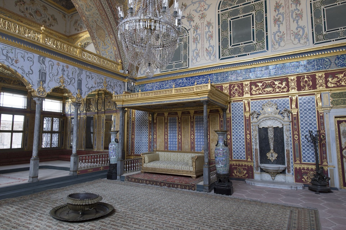 The Imperial Hall in the Harem of Topkapı Palace: a canopied throne against blue-and-white tiled walls, gilded friezes and a crystal chandelier