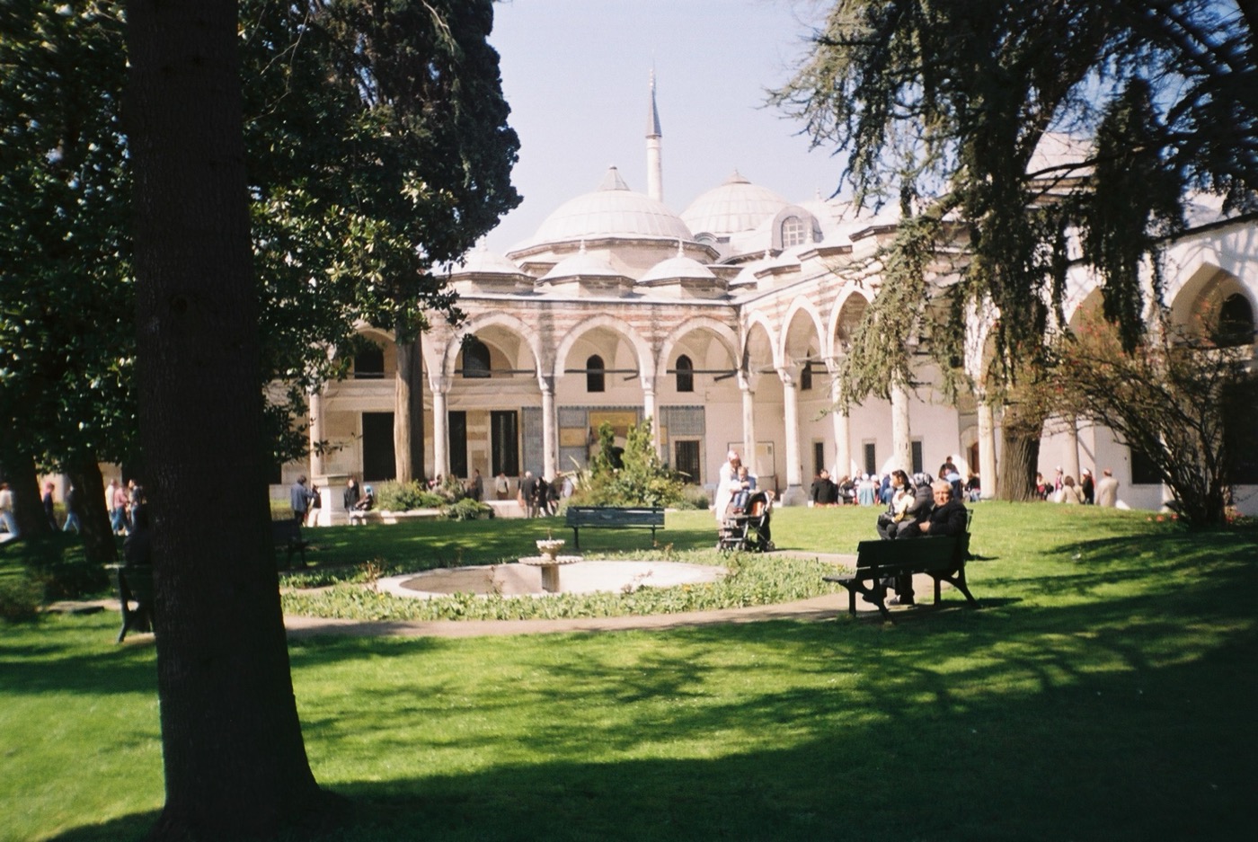 The Third Courtyard of Topkapı Palace with lawns, benches and visitors in front of a colonnaded pavilion