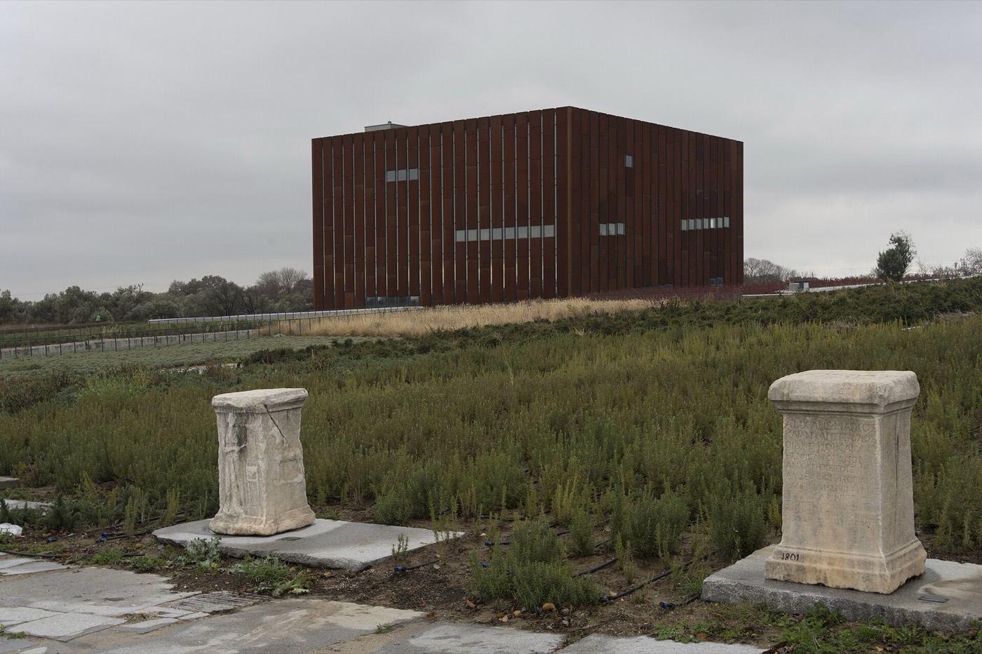 The rust-coloured cube of the Troy Museum standing in the fields, with two ancient columns in front