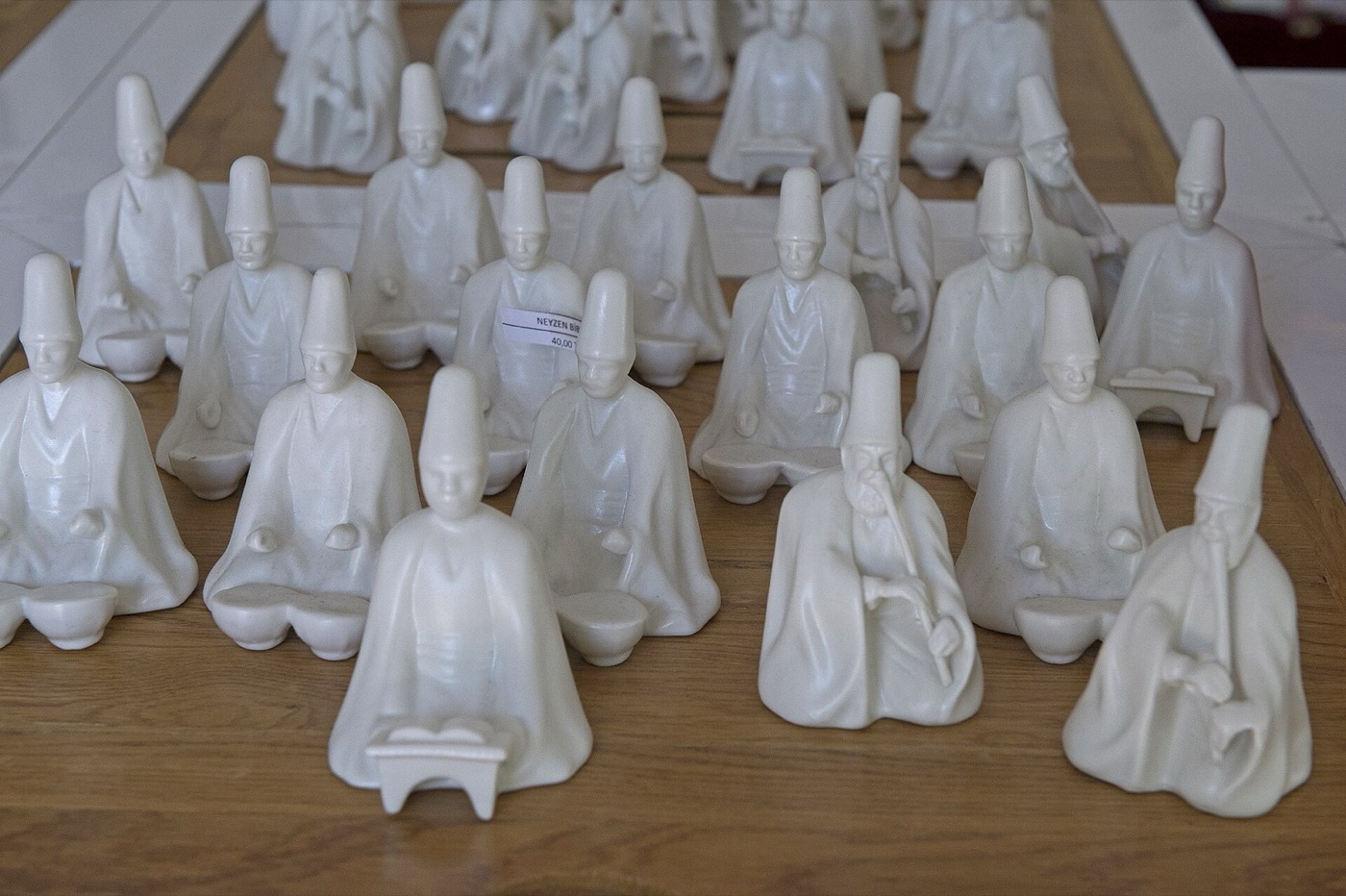 Rows of white porcelain figures of seated dervishes on a wooden table at a Yıldız Porcelain sales point