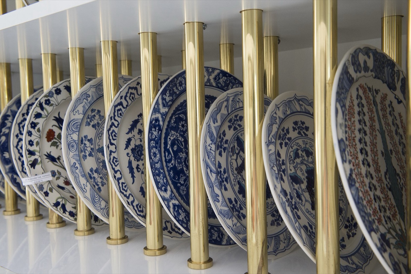 Yıldız Porcelain plates with blue-and-white and coloured floral patterns standing in a brass display rack